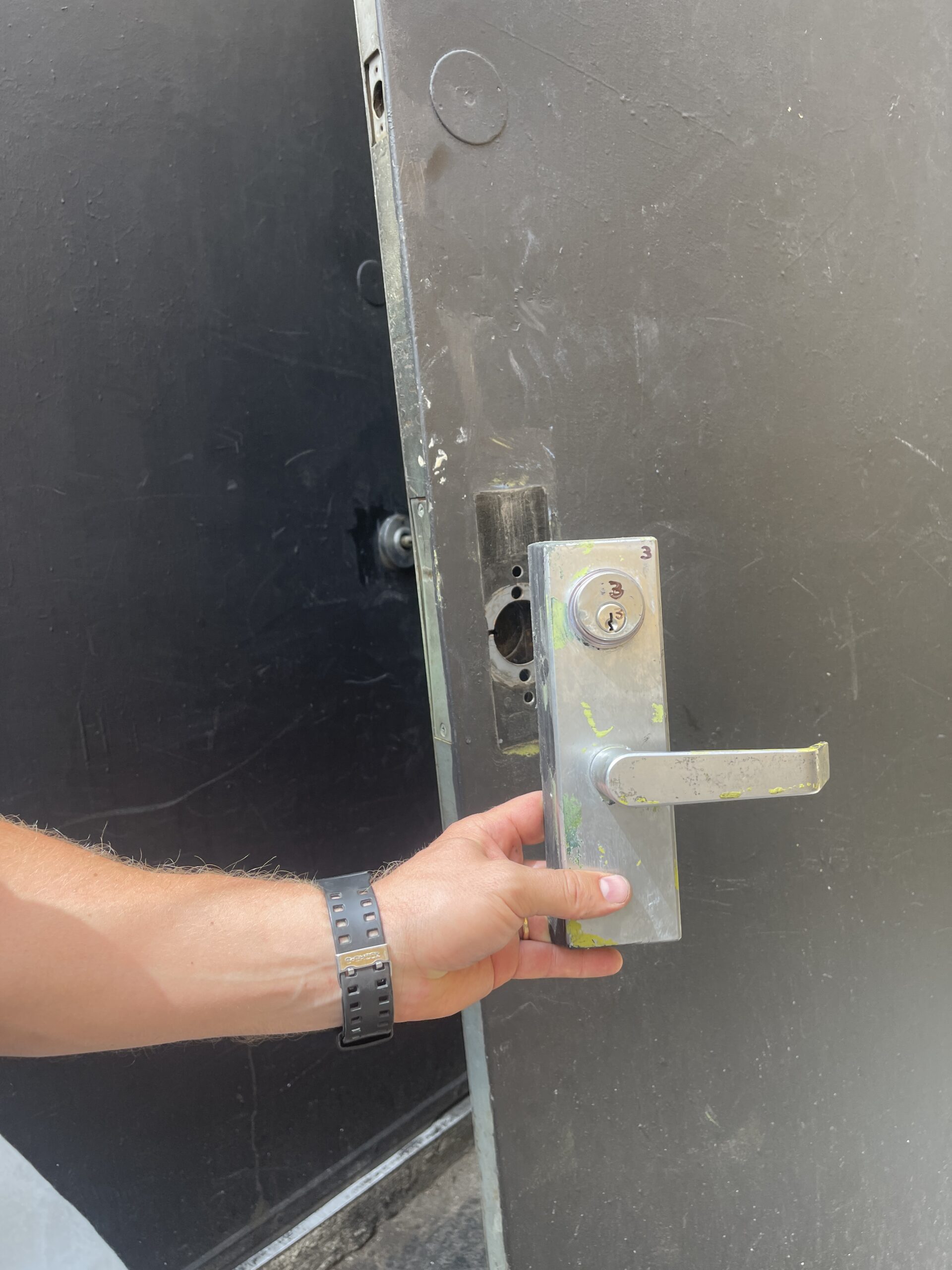A person removing a commercial door lock with a screwdriver
